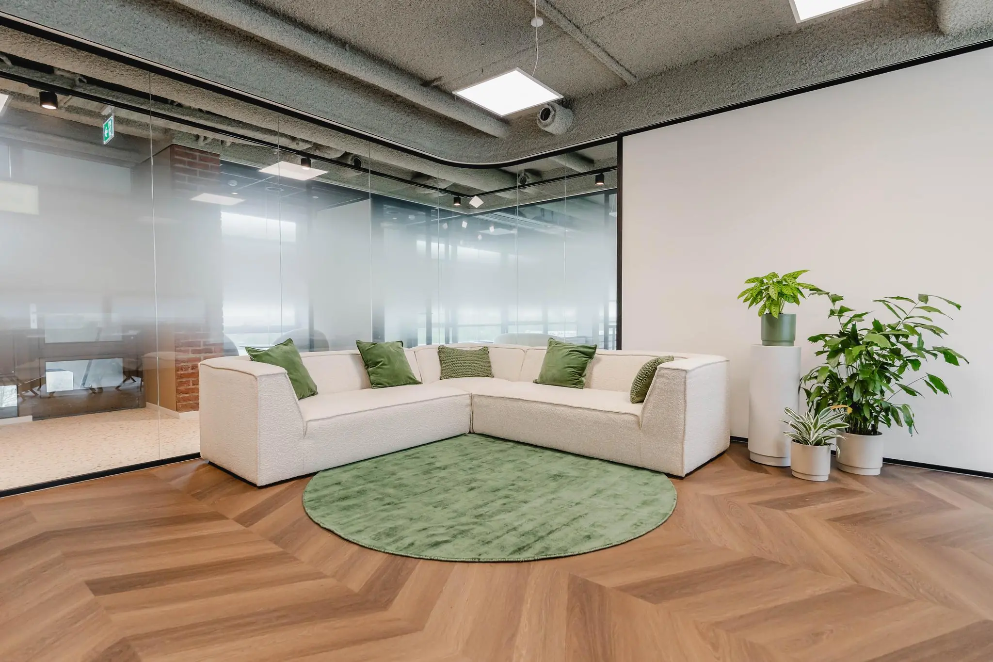 Moderne loungehoek met witte hoekbank, groene kussens, planten en een groen vloerkleed in een kantoor aan de Joop Geesinkweg.